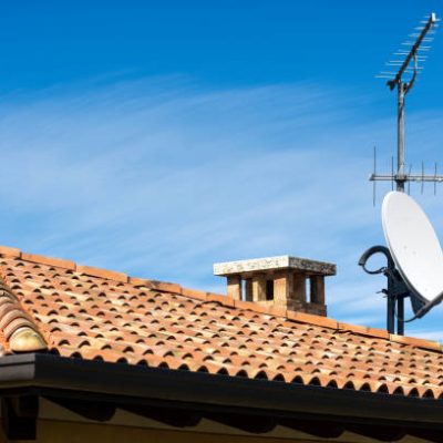 Closeup of a Television Aerial and Satellite Dish on the House Roof on blue sky with clouds